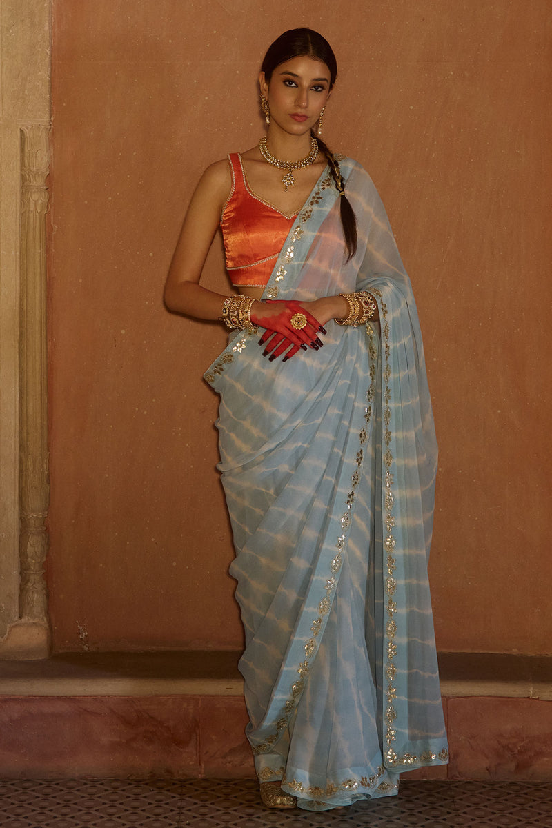 Neelima – Sky Blue Leheriya Saree with Orange Sleeveless  Blouse