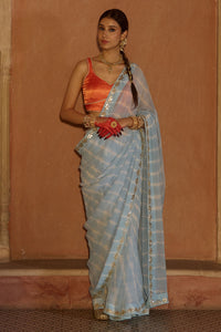 Neelima – Sky Blue Leheriya Saree with Orange Sleeveless  Blouse