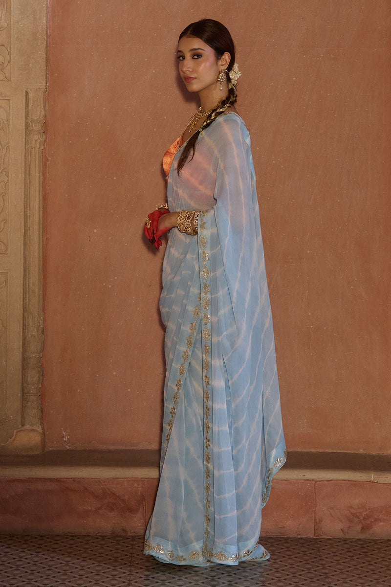 Neelima – Sky Blue Leheriya Saree with Orange Sleeveless  Blouse