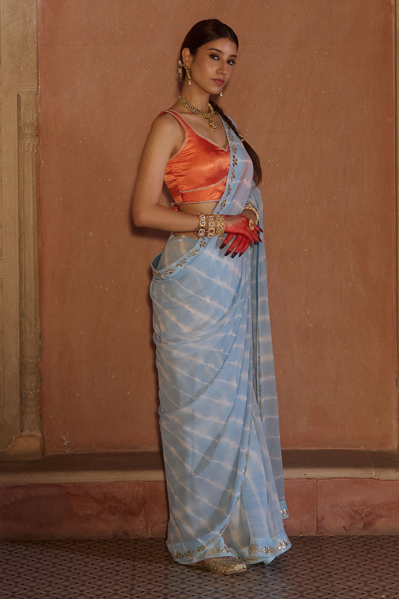 Neelima – Sky Blue Leheriya Saree with Orange Sleeveless  Blouse